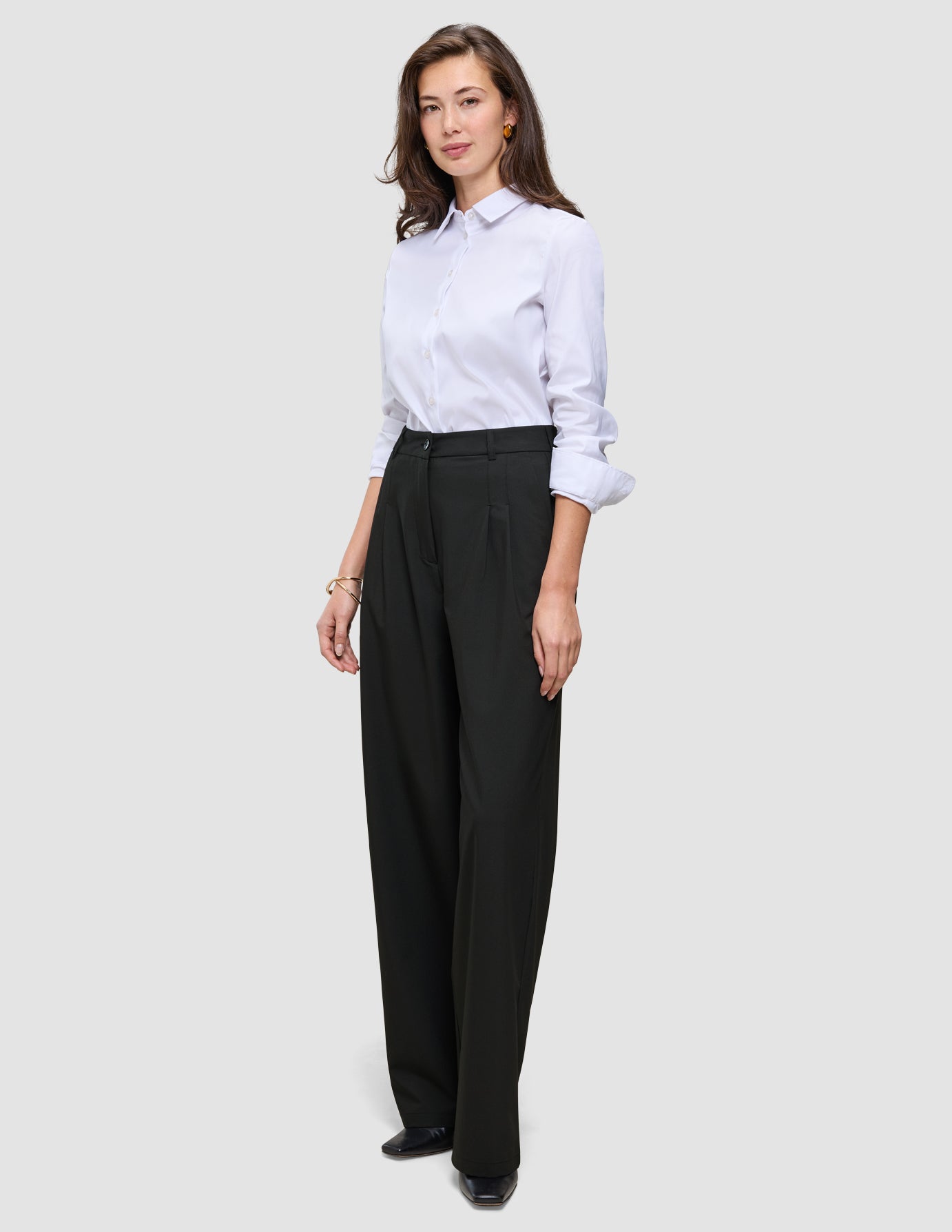 En kvinne har på seg en hvit skjorte med knapper og svarte Avira-bukser i bred modell for kvinner.