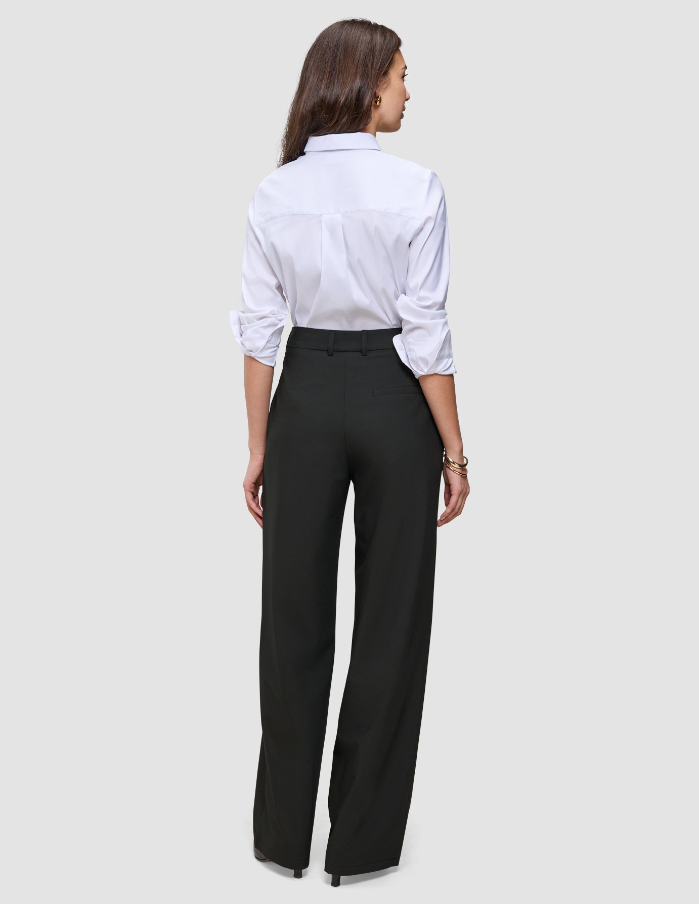 En kvinne sett bakfra, iført en hvit skjorte med knapper og svarte Women’s Avira Pants Wide Black-bukser med høy midje.