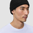 En person som har på seg en svart Beanie Black-lue i et skandinavisk ribbestrikket mønster.