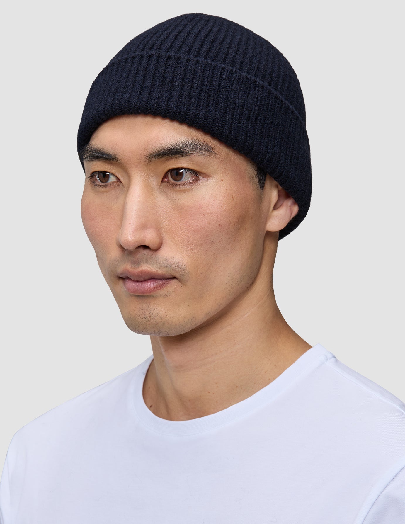 En mann som har på seg en marineblå Wool Beanie Navy i ribbestrikket design.