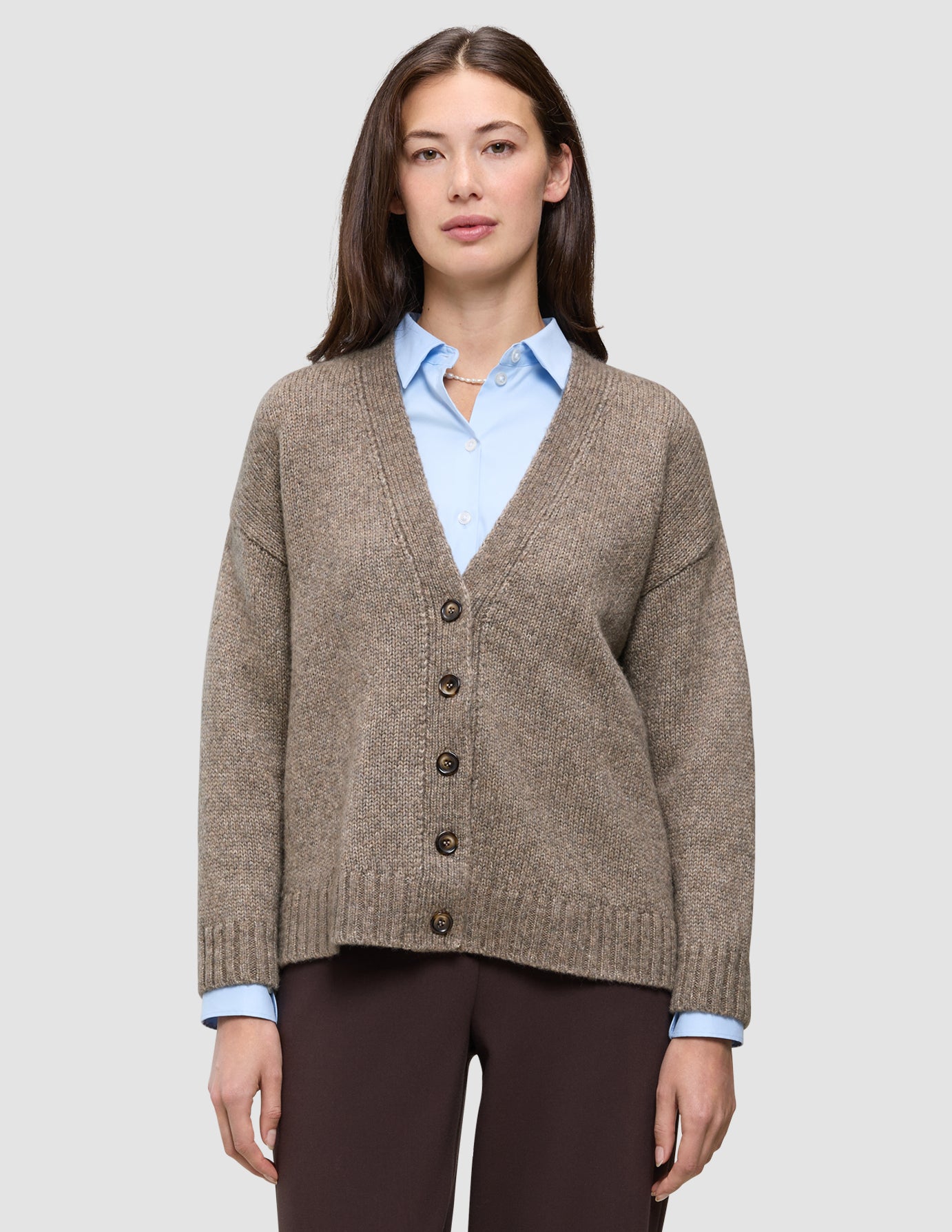 En tykk, myk strikket cardigan i ull for damer i fargen taupe melange, båret over en lyseblå skjorte med krage i klassisk dansk design.