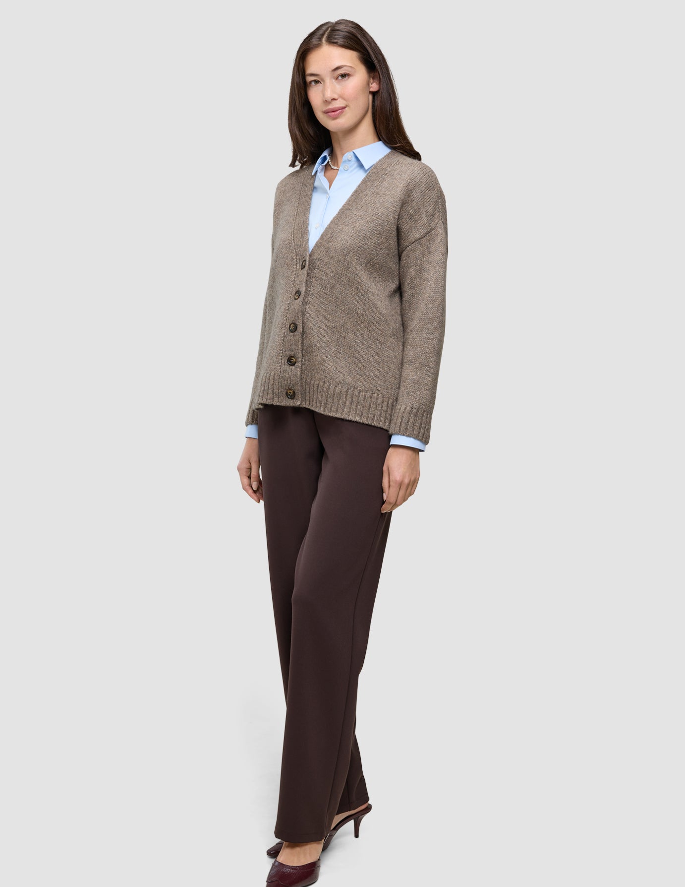 En kvinne som har på seg en Women’s Chunky Soft Wool Knit Cardigan Taupe Melange over en lyseblå skjorte og mørke bukser.