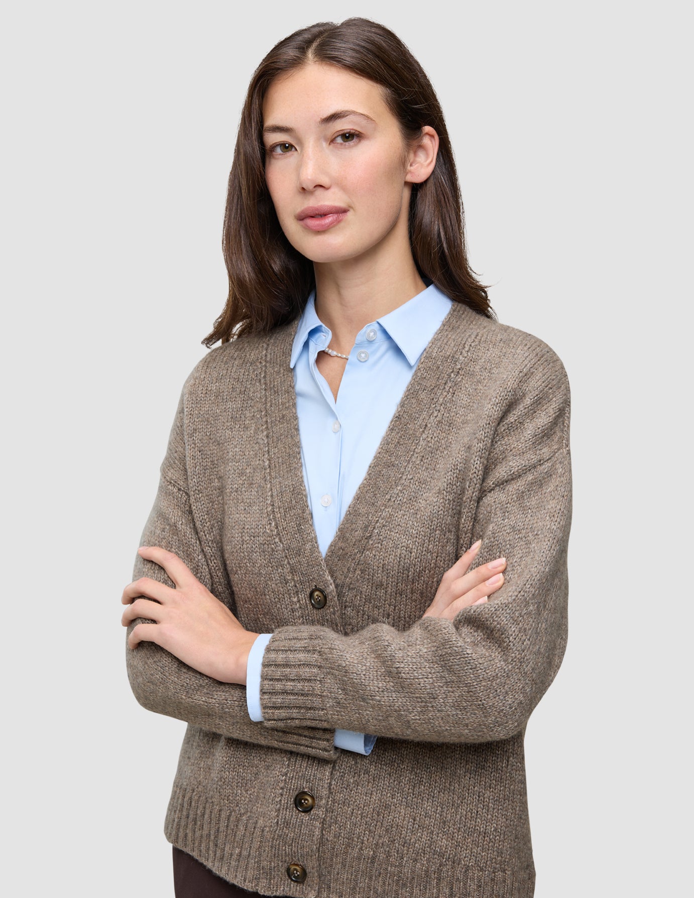 En kvinne som har på seg en tykk, myk ullstrikket cardigan for damer i fargen taupe melange over en lyseblå skjorte med krage.