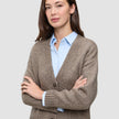 En kvinne som har på seg en tykk, myk ullstrikket cardigan for damer i fargen taupe melange over en lyseblå skjorte med krage.