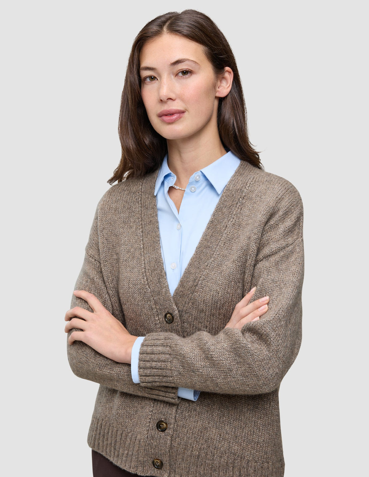 En kvinne som har på seg en tykk, myk ullstrikket cardigan for damer i fargen taupe melange over en lyseblå skjorte med krage.