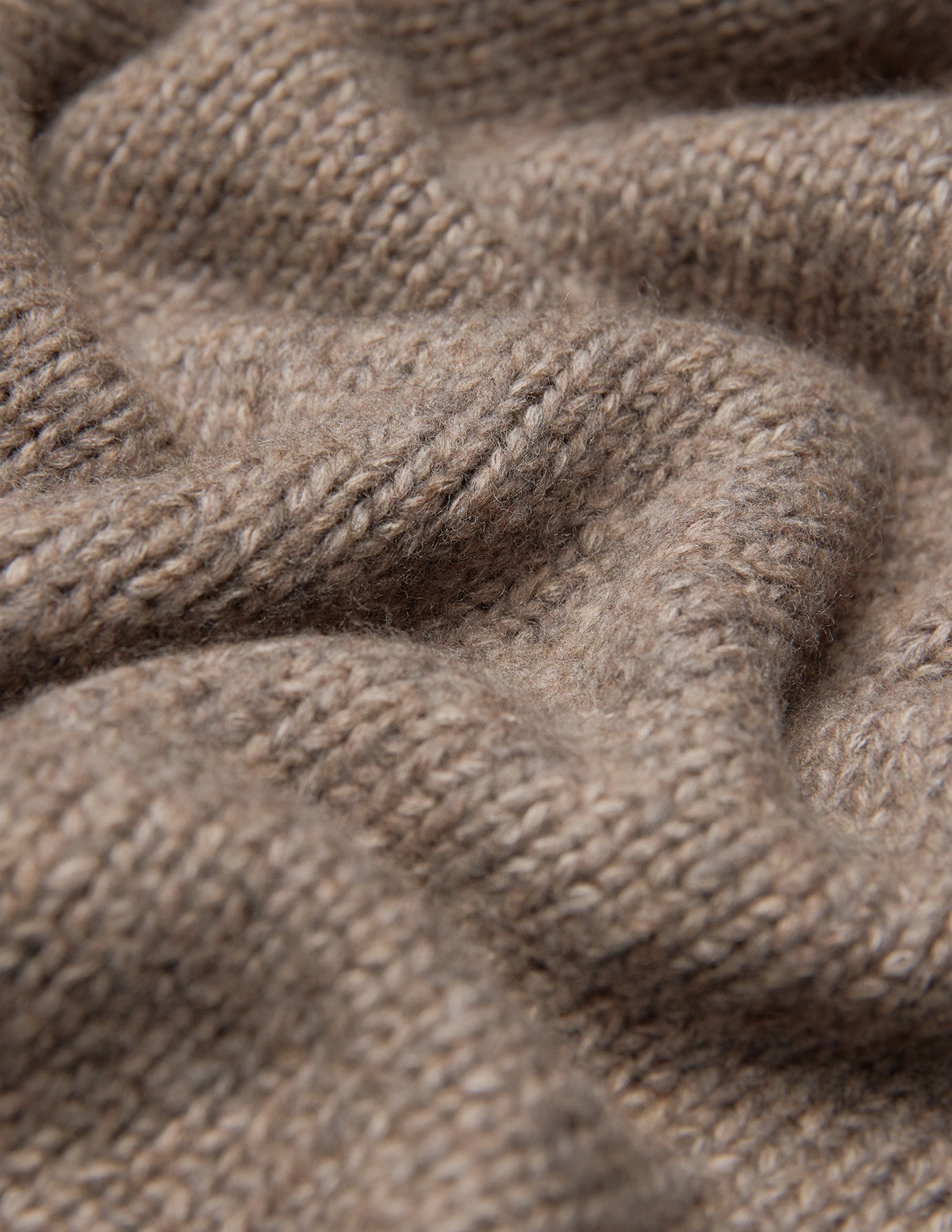 Nærbilde av en tykk, myk strikket damekardigan i taupe-melange, med en tykk, ribbet struktur i beige.
