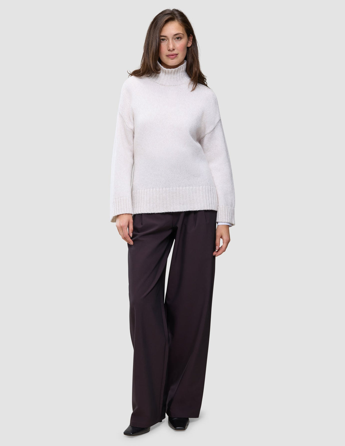 En kvinne kledd i en Women’s Chunky Soft Wool Knit Turtleneck Sugar Melange og mørke bukser med vide ben.