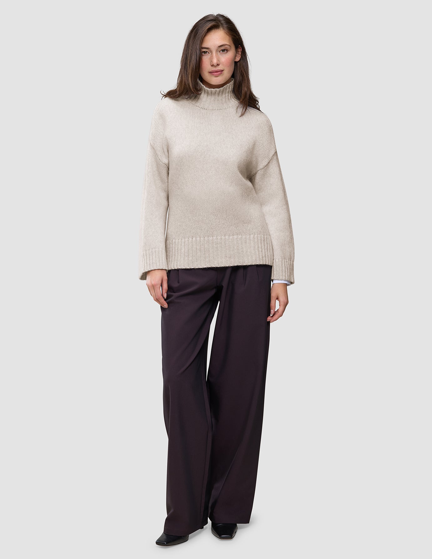 En kvinne har på seg en Women’s Chunky Soft Wool Knit Turtleneck Sugar Melange-genser og mørke bukser med vide ben.
