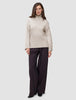 En kvinne har på seg en Women’s Chunky Soft Wool Knit Turtleneck Sugar Melange-genser og mørke bukser med vide ben.