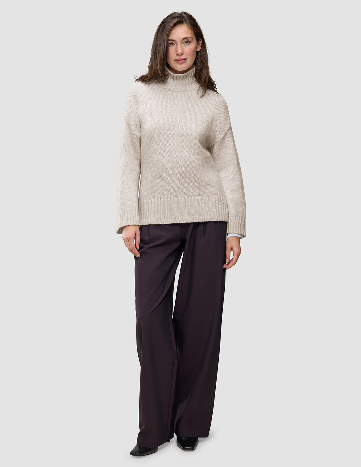En kvinne har på seg en Women’s Chunky Soft Wool Knit Turtleneck Sugar Melange-genser og mørke bukser med vide ben.