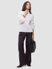 En kvinne kledd i en Women’s Chunky Soft Wool Knit Turtleneck Sugar Melange og mørke bukser med vide ben, som holder en svart håndveske.