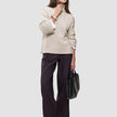 En kvinne har på seg en Women’s Chunky Soft Wool Knit Turtleneck Sugar Melange over en hvit skjorte og mørke bukser med vide ben.