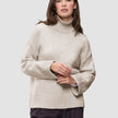En kvinne iført en Women’s Chunky Soft Wool Knit Turtleneck Sugar Melange, en oversized, lysbeige ribbestrikket turtleneck.