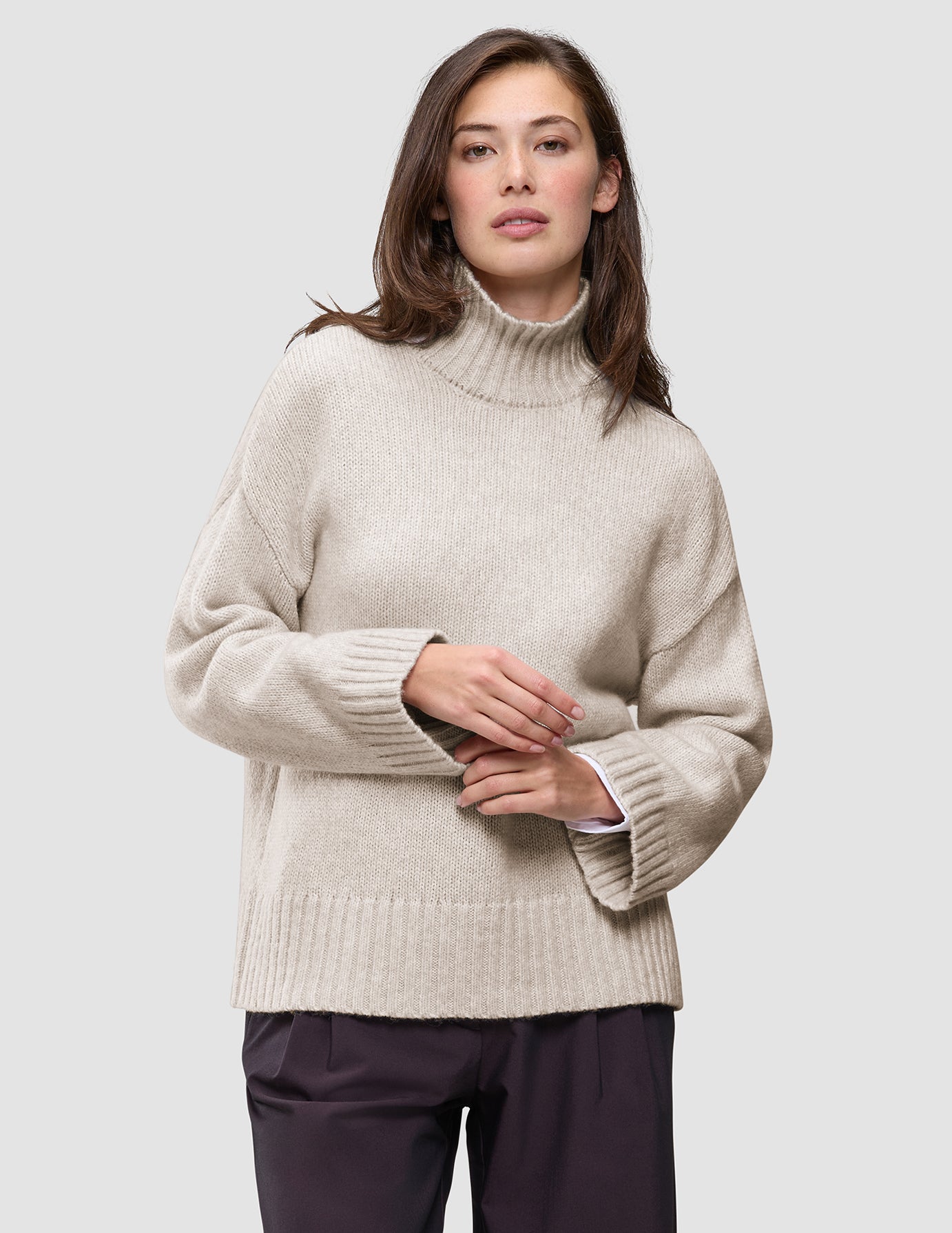 En kvinne iført en Women’s Chunky Soft Wool Knit Turtleneck Sugar Melange, en oversized, lysbeige ribbestrikket turtleneck.