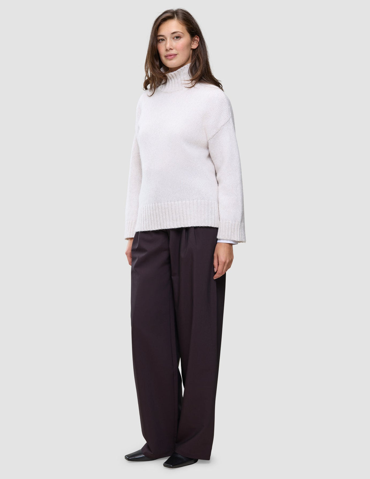 En kvinne kledd i en Women’s Chunky Soft Wool Knit Turtleneck Sugar Melange og mørke bukser med vide ben.
