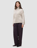 En kvinne kledd i en beige Women’s Chunky Soft Wool Knit Turtleneck Sugar Melange-genser og mørke bukser med vide ben.