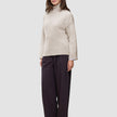 En kvinne kledd i en beige Women’s Chunky Soft Wool Knit Turtleneck Sugar Melange-genser og mørke bukser med vide ben.