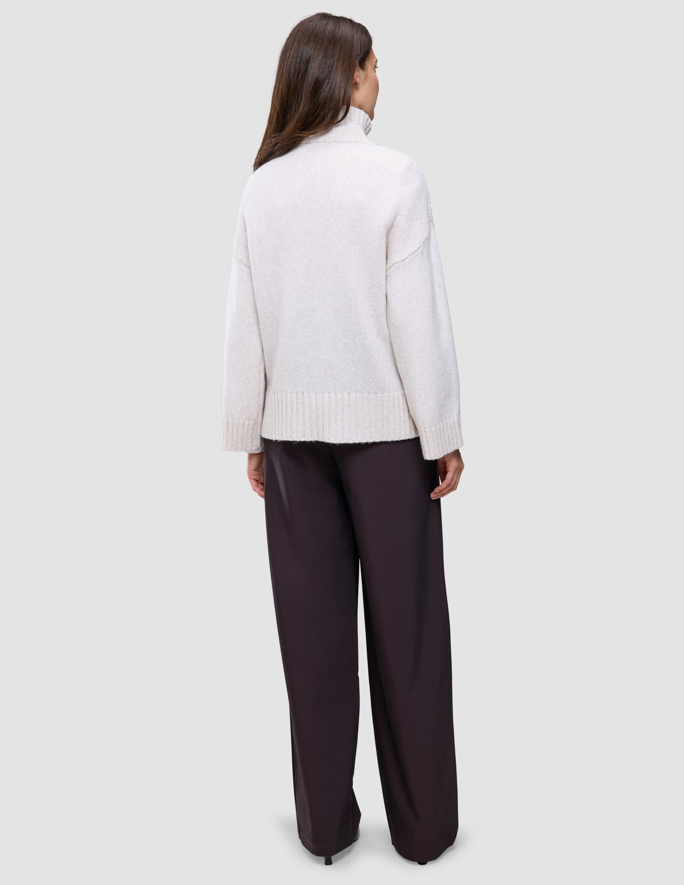 Bakfra-bilde av en person iført en tykk, myk damestrikket turtleneck i Sugar Melange og mørke bukser med vide ben.