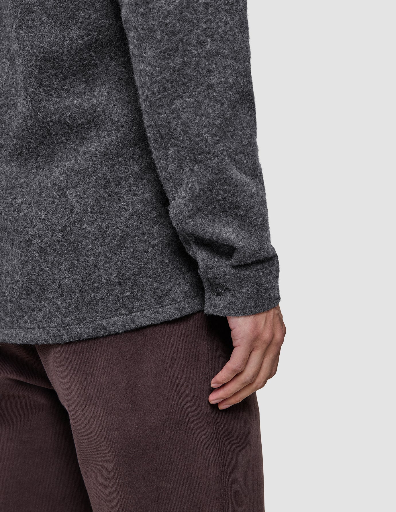 Nærbilde av en person som har på seg en mørkegrå Double Layer Wool Overshirt Regular og brune bukser.