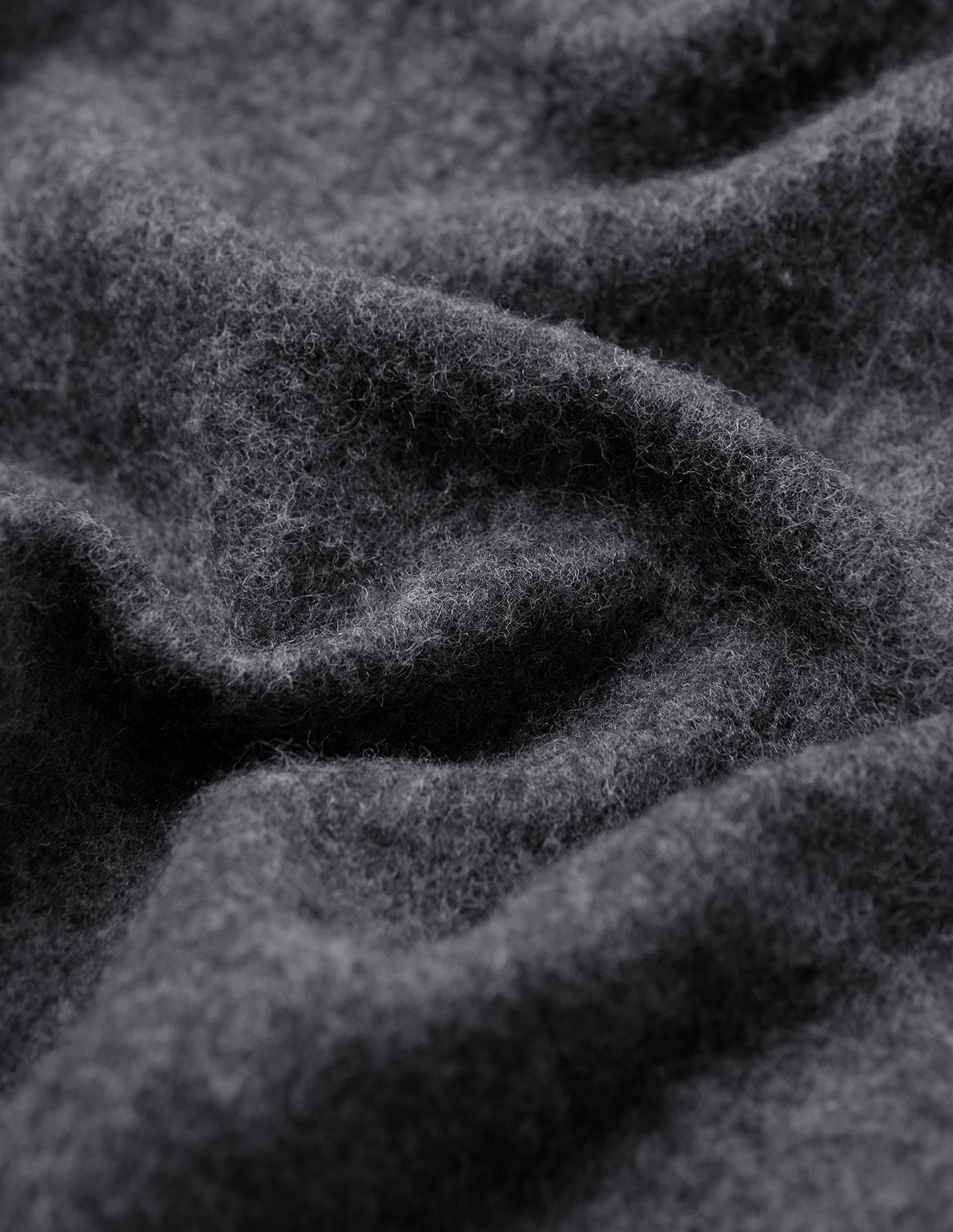 Nærbilde av en brettet, mørkegrå Double Layer Wool Overshirt Regular Dark Grey-skjorte i et stoff med en lodden tekstur.