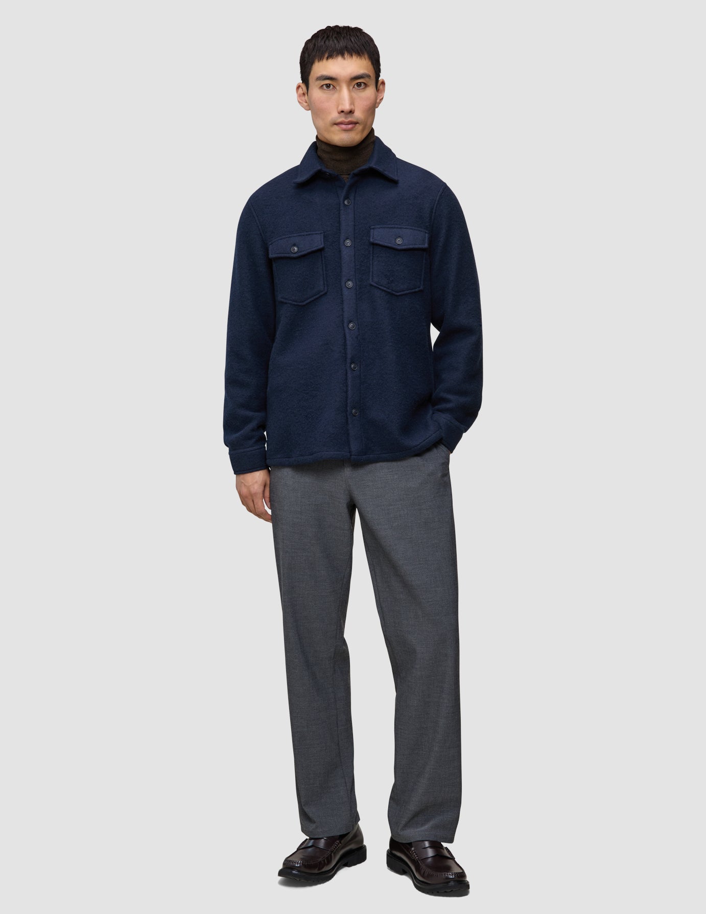 En mann har på seg en dobbeltsidig ullskjorte i mørk marineblå i standardpassform over en brun turtleneck og grå bukser.