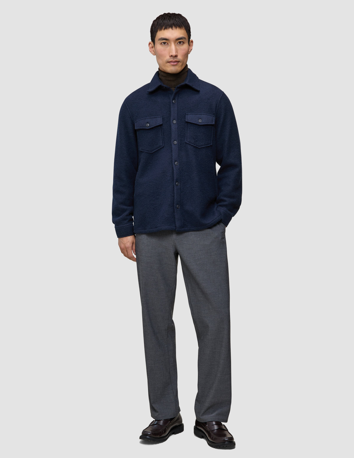 En mann har på seg en dobbeltsidig ullskjorte i mørk marineblå i standardpassform over en brun turtleneck og grå bukser.