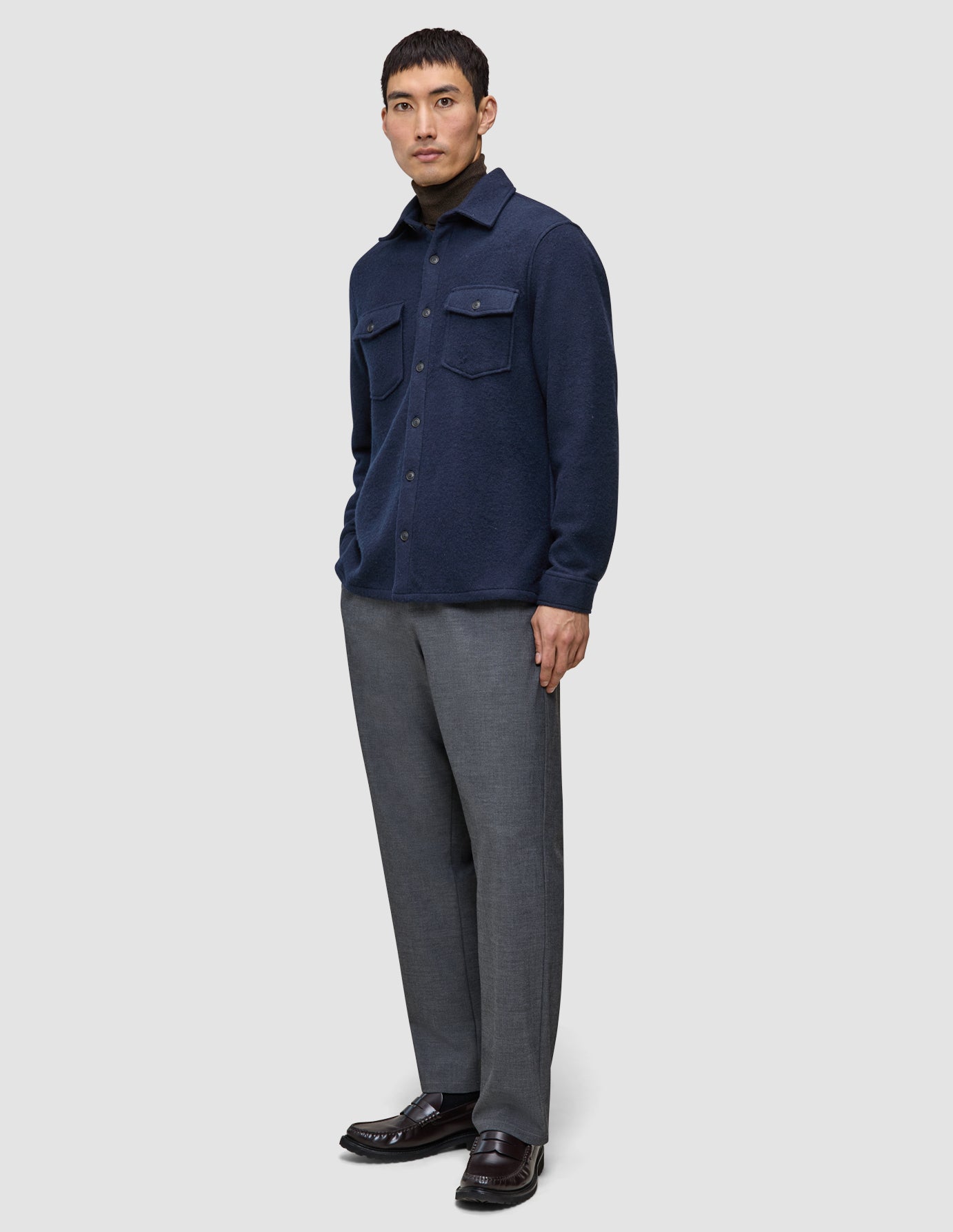 En person iført en dobbeltsidig ullskjorte i mørk marineblå i regular-passform, brun turtleneck, grå bukser og mørke loafers.
