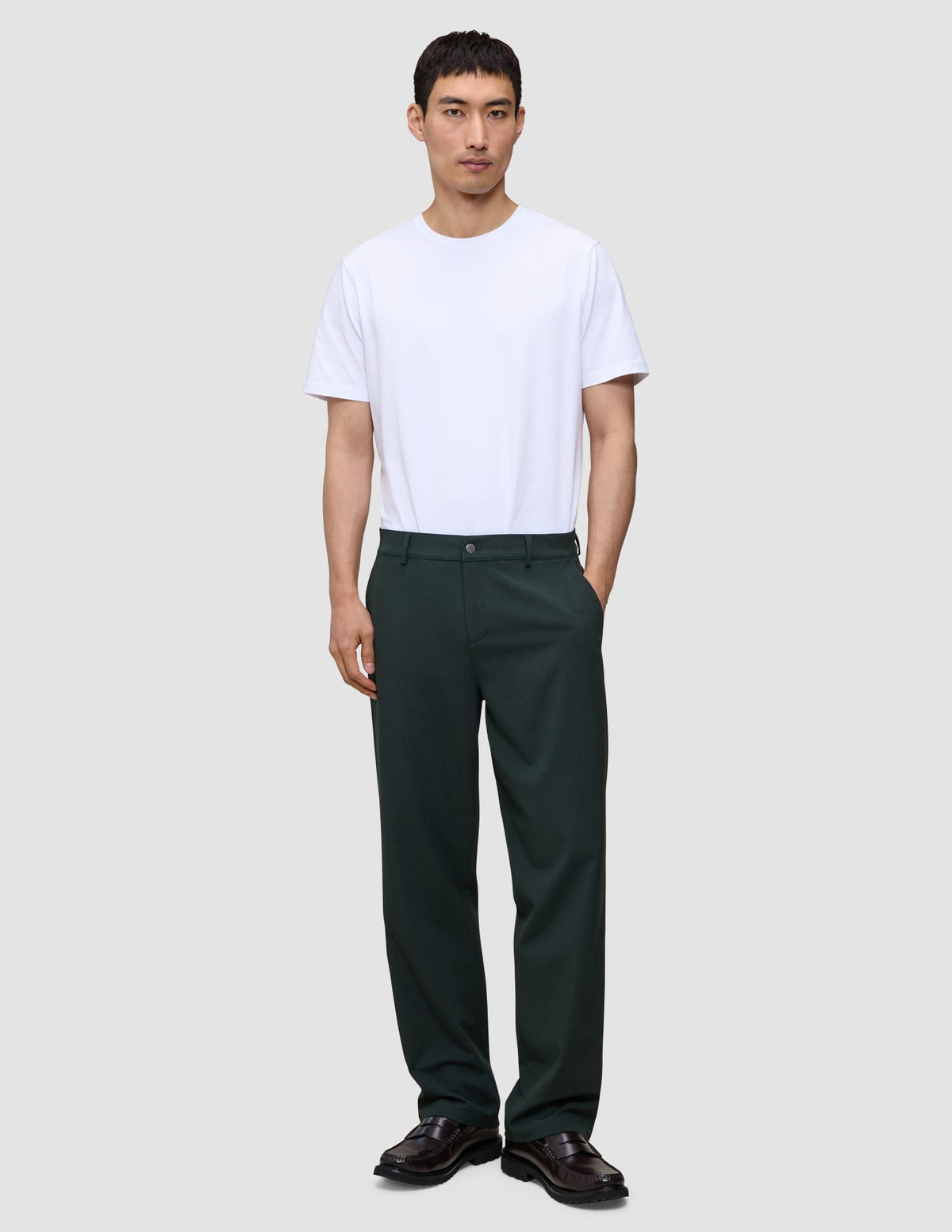 En person i en hvit T-skjorte, mørkegrønne Ease Pants Relaxed Fit Northern Pine og mørke loafers.