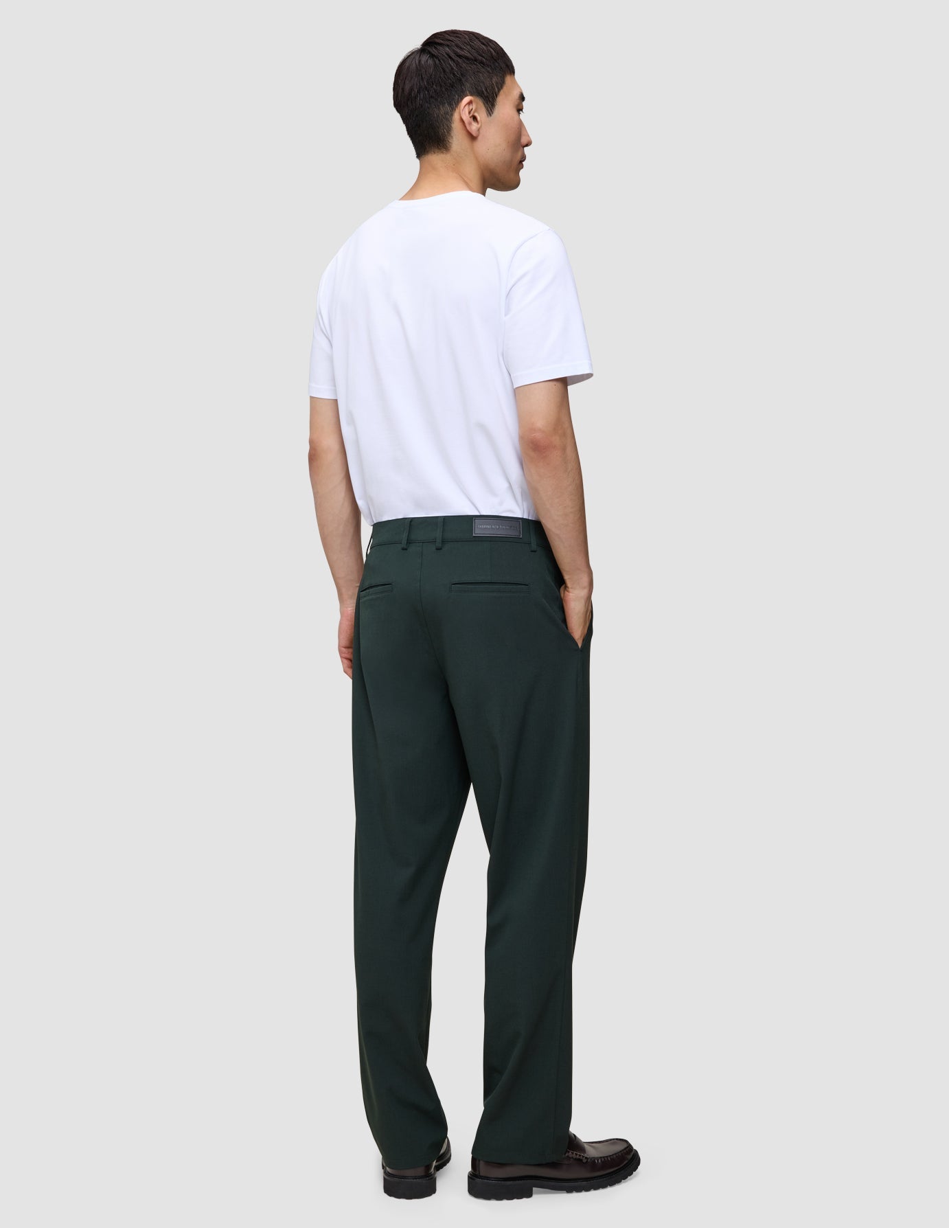 En mann sett bakfra, kledd i en hvit T-skjorte og mørkegrønne Ease Pants Relaxed Fit Northern Pine med 360°-stretch.