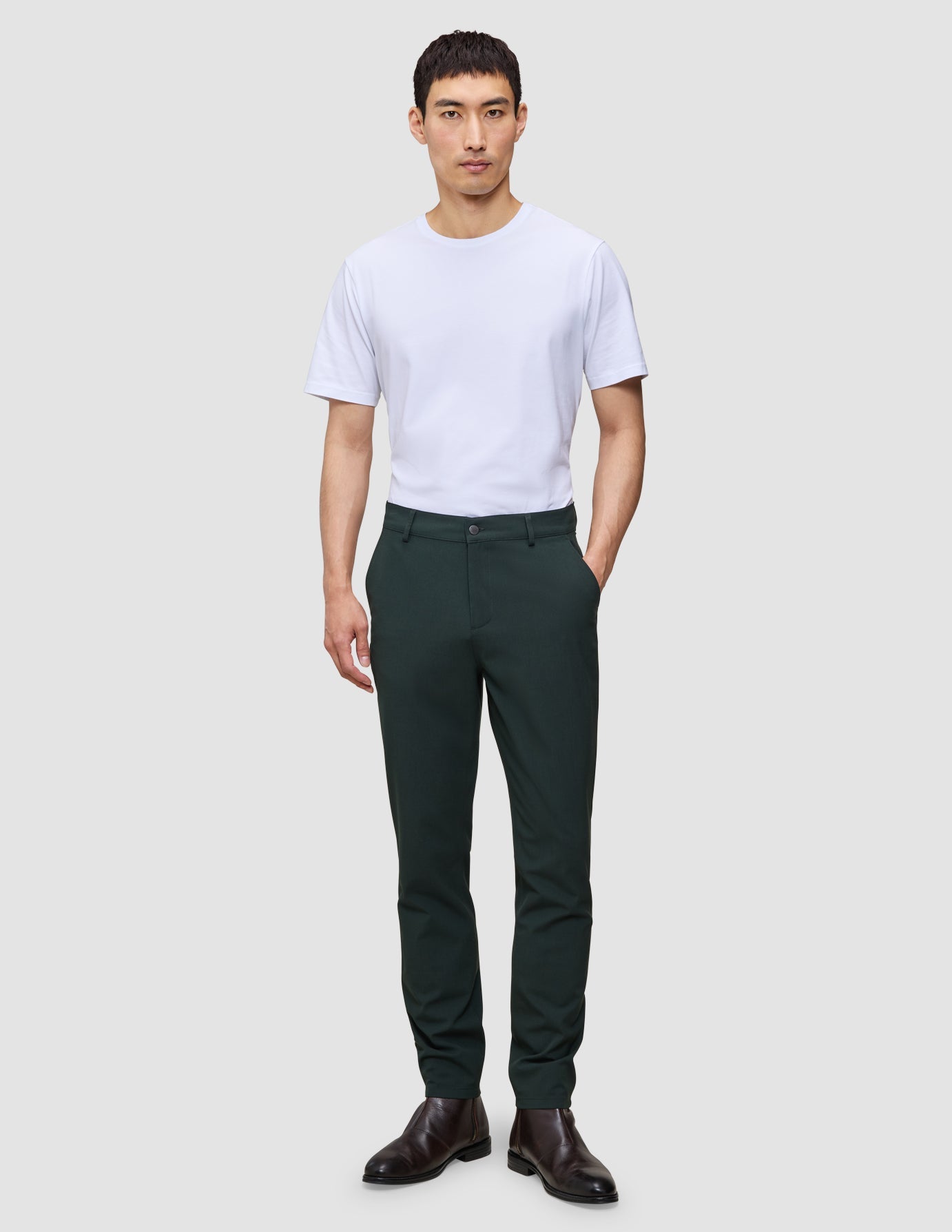 En mann i en hvit T-skjorte, Ease Pants Slim Northern Pine og mørkebrune skinnstøvler.