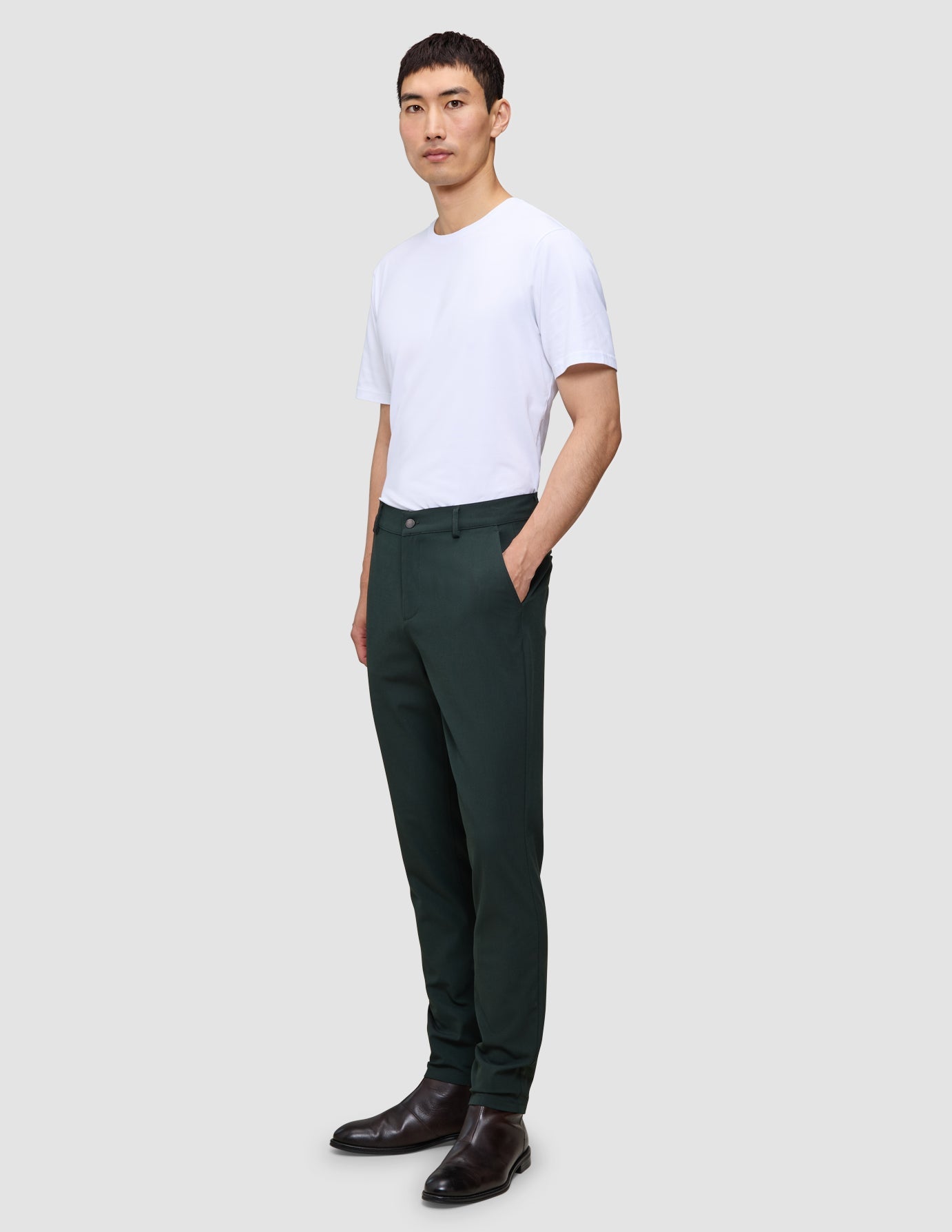 En person i en hvit T-skjorte, Ease Pants Slim Northern Pine og mørke lærstøvler i skandinavisk design.