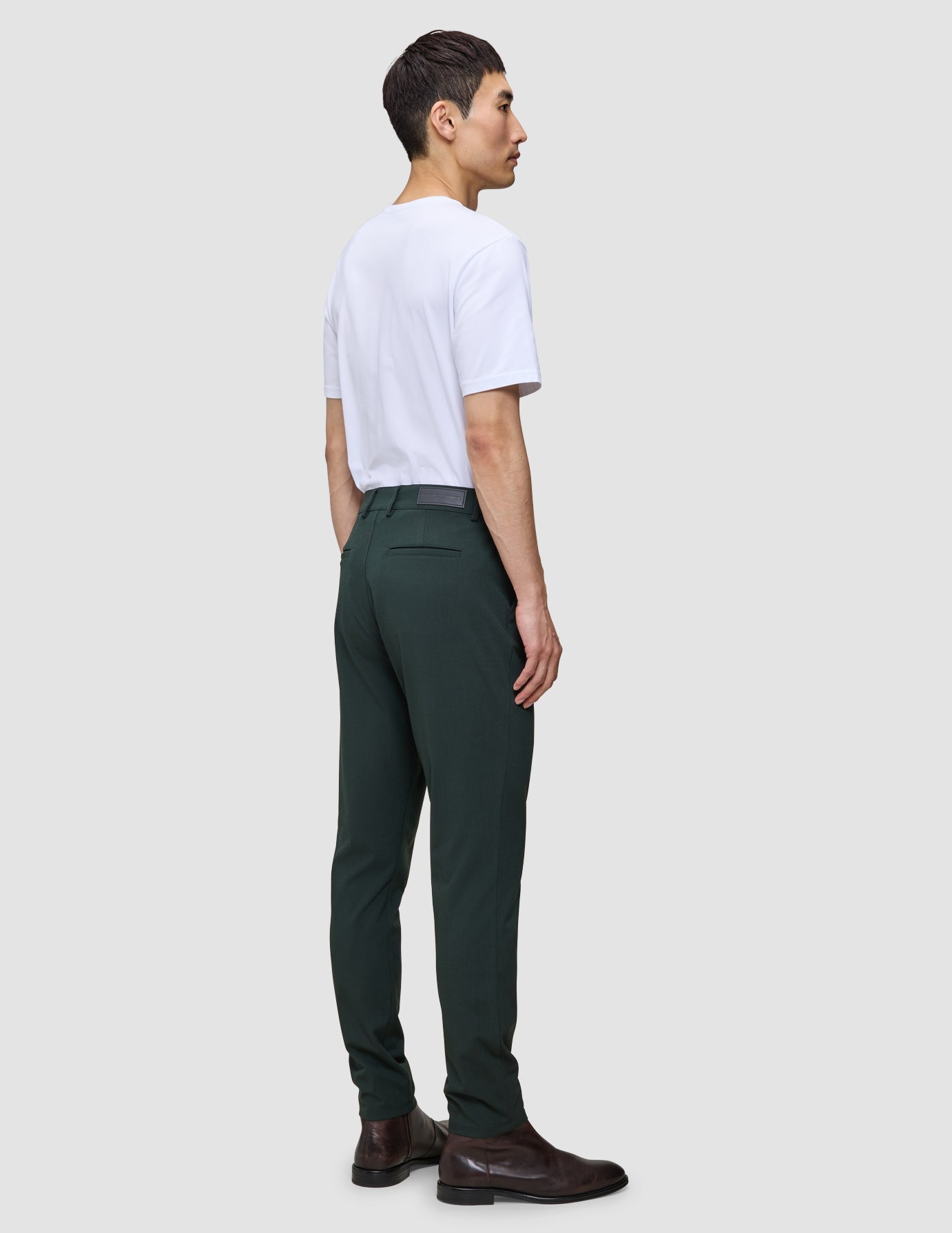 En mann sett i profil har på seg en hvit T-skjorte, Ease Pants Slim Northern Pine og brune lærstøvler, som fremhever det skandinaviske designet.