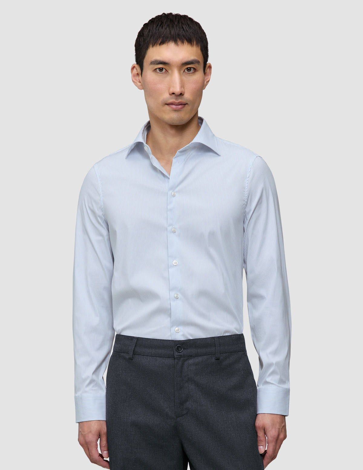 En mann kledd i en Elevated Shirt Regular Classic Blue Striped – en lyseblå og hvit stripete bomullsskjorte – og grå bukser.