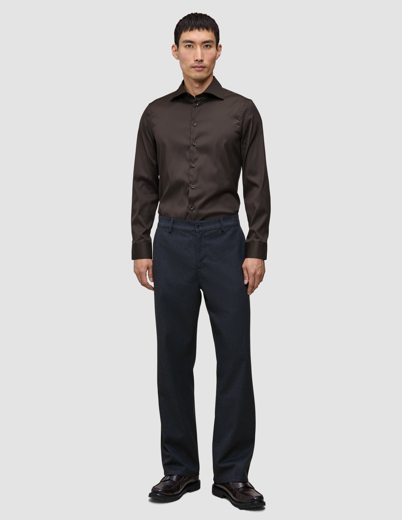 En mann i en Elevated Shirt Regular i mørkebrunt, mørke bukser og skinnsko – et uttrykk for skandinavisk design.