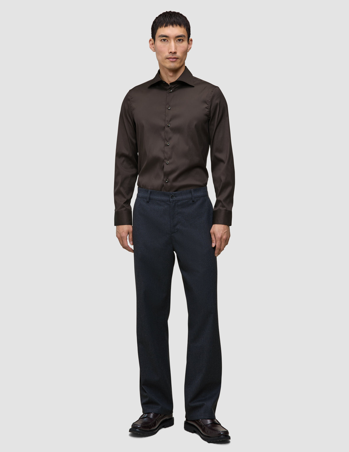 En mann i en Elevated Shirt Regular i mørkebrunt, mørke bukser og skinnsko – et uttrykk for skandinavisk design.