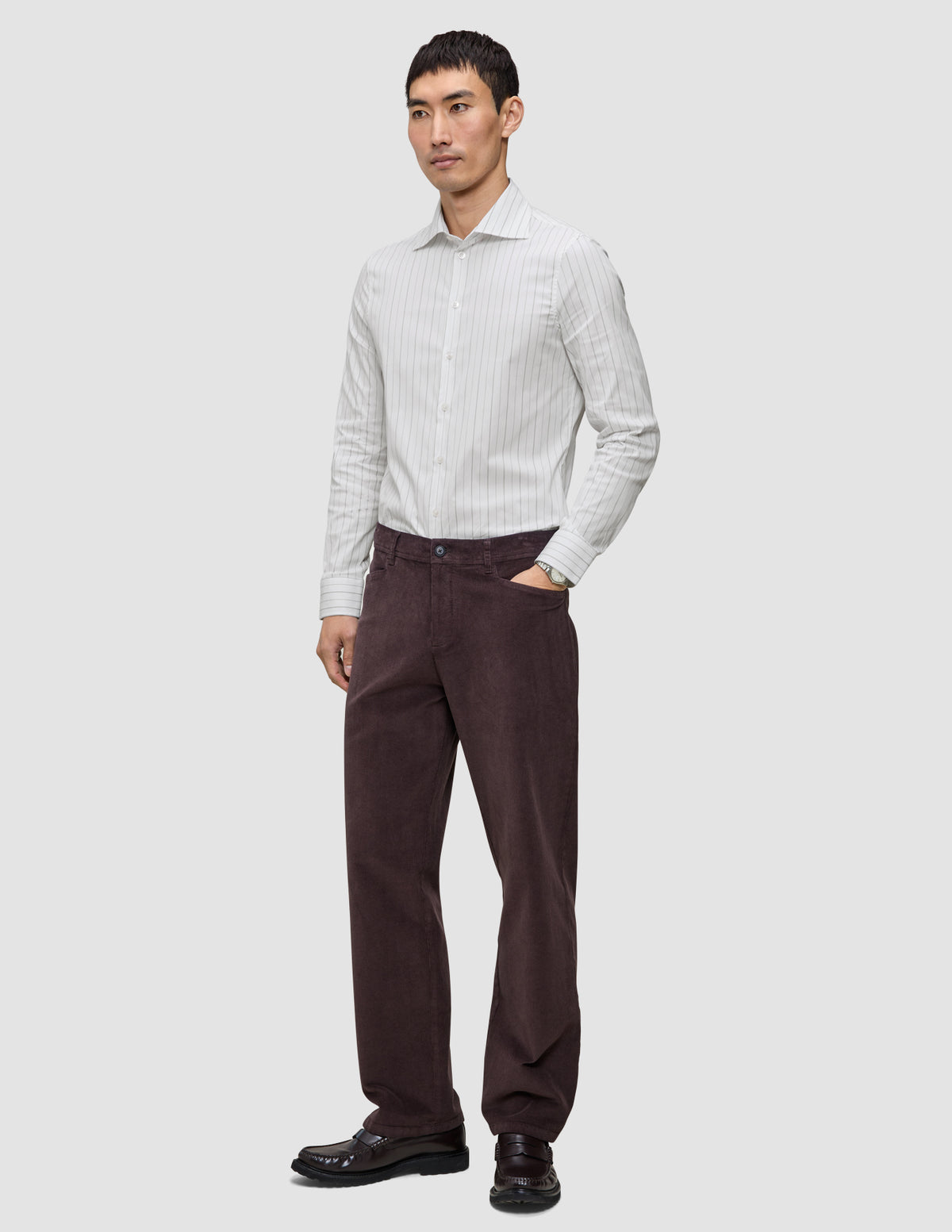 En mann kledd i en Elevated Shirt Regular Light Grey Striped-skjorte og mørkebrune bukser.