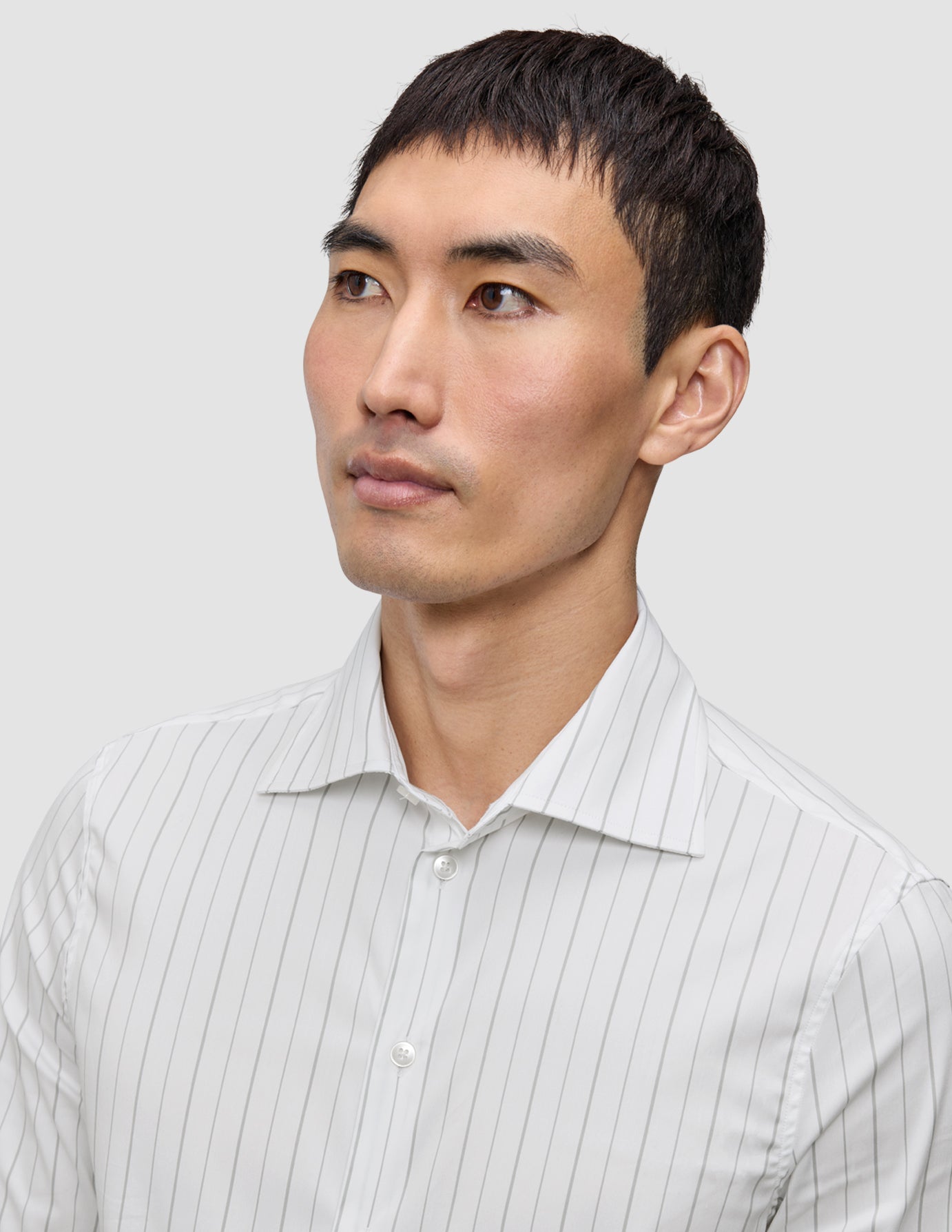 En mann kledd i en Elevated Shirt Regular Light Grey Striped, en elegant hvit skjorte med tynne, grå vertikale striper.
