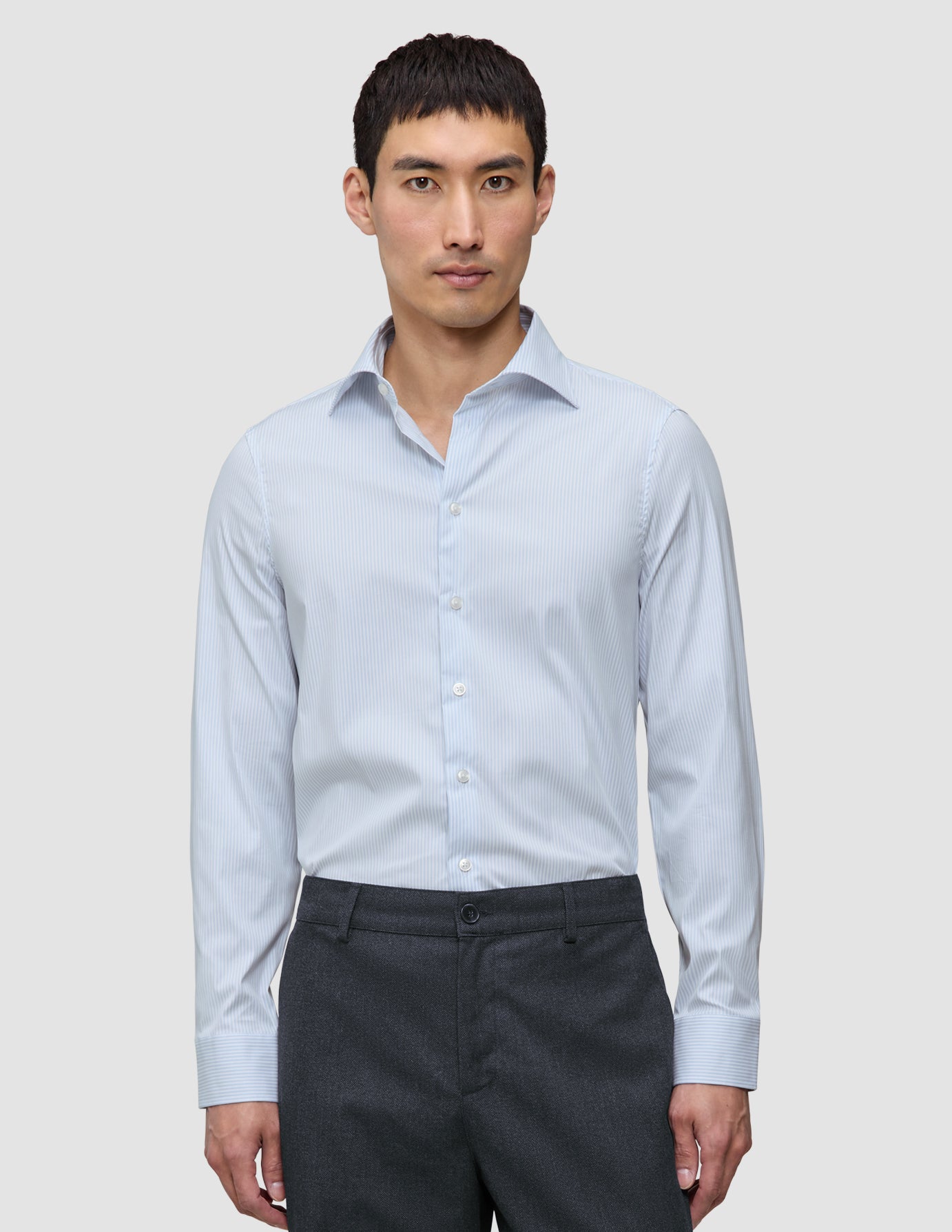 En mann iført en Elevated Shirt Slim Classic Blue Striped i lyseblått og hvitt, som er stappet inn i mørkegrå bukser.