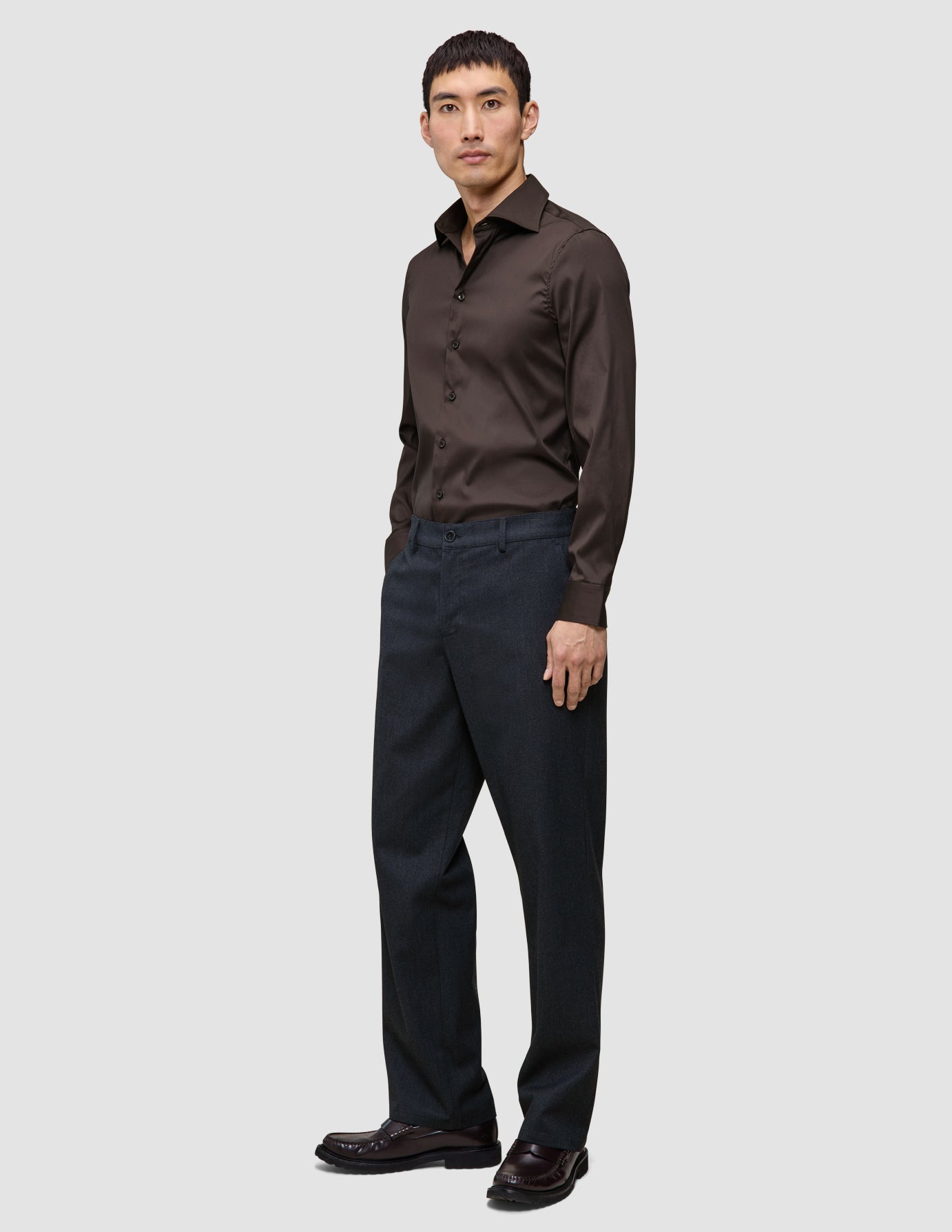 En mann kledd i en mørkebrun Elevated Shirt Slim-skjorte i pima-bomull og antrasittgrå bukser.