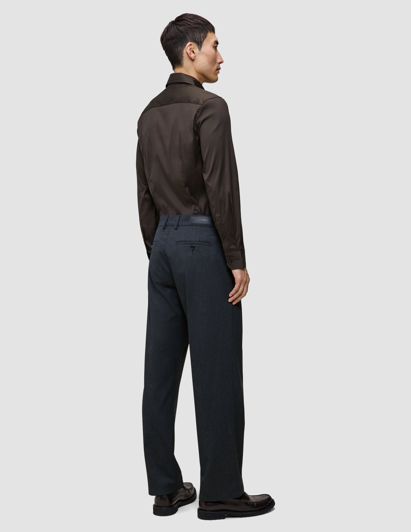 Bakfra-bilde av en mann som har på seg en mørkebrun Elevated Shirt Slim, stappet inn i mørkegrå bukser og mørke skinnsko.