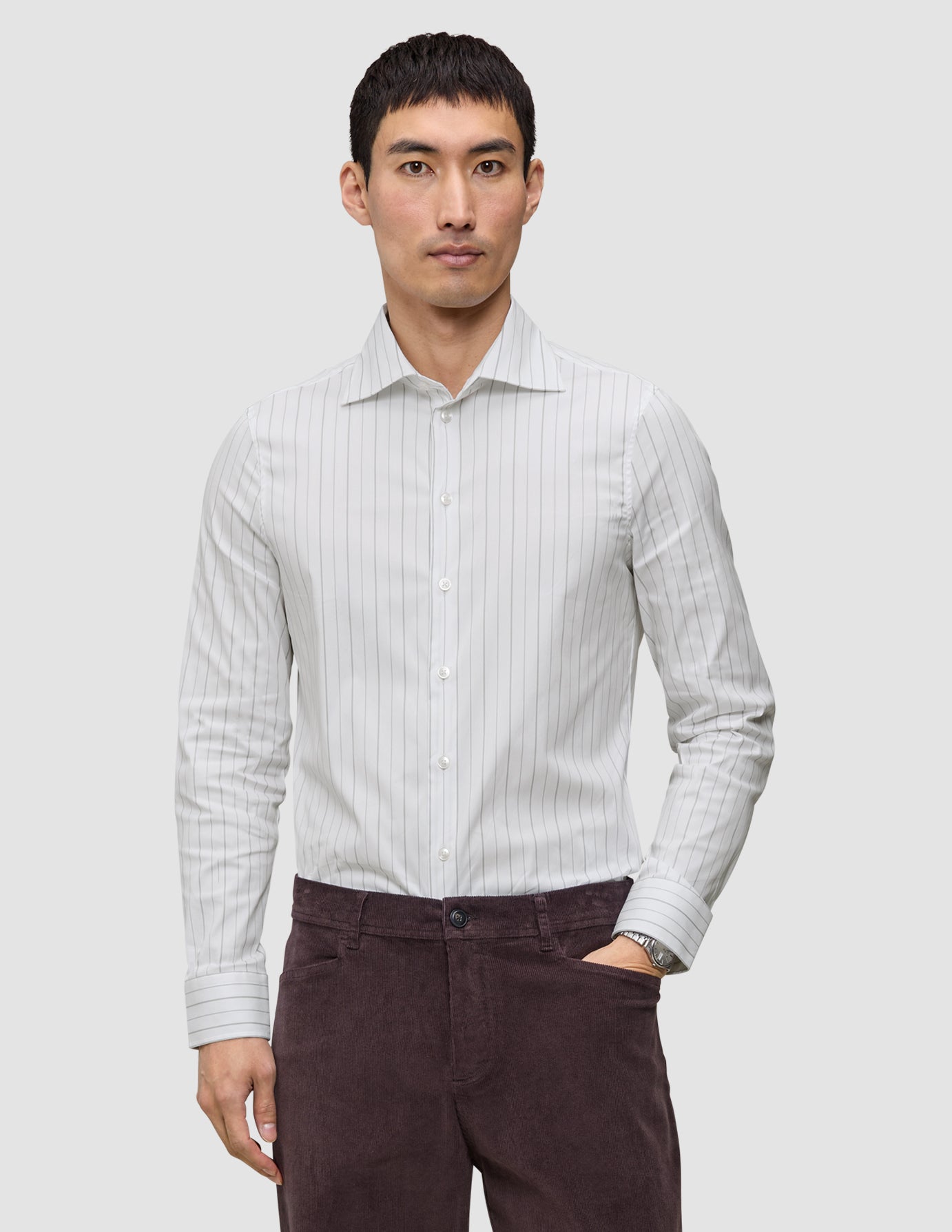En mann kledd i en Elevated Shirt Slim Light Grey Striped-skjorte med knapper og mørke bukser.
