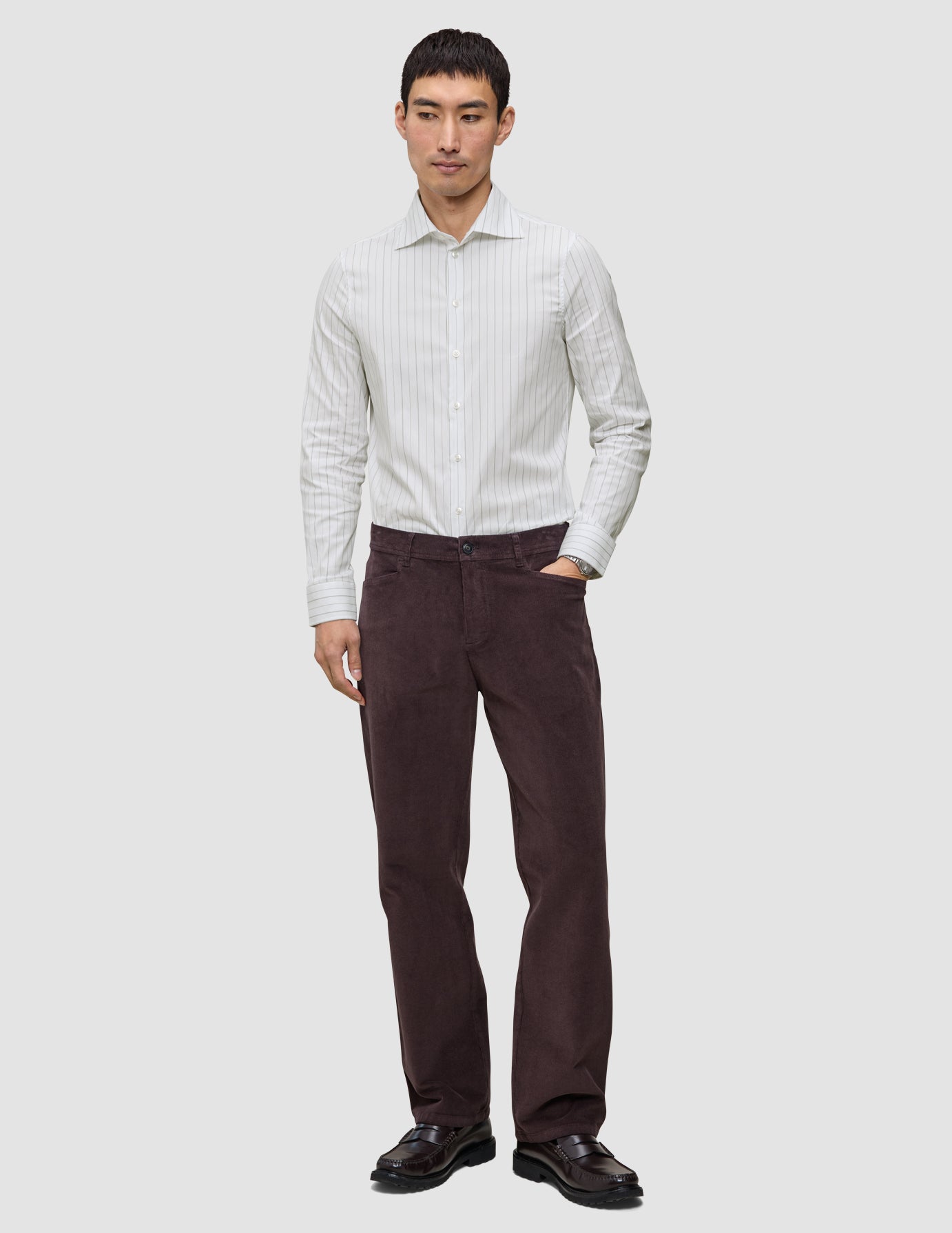 En mann i en Elevated Shirt Slim med lysegrå striper, mørke bukser og mørke loafers.