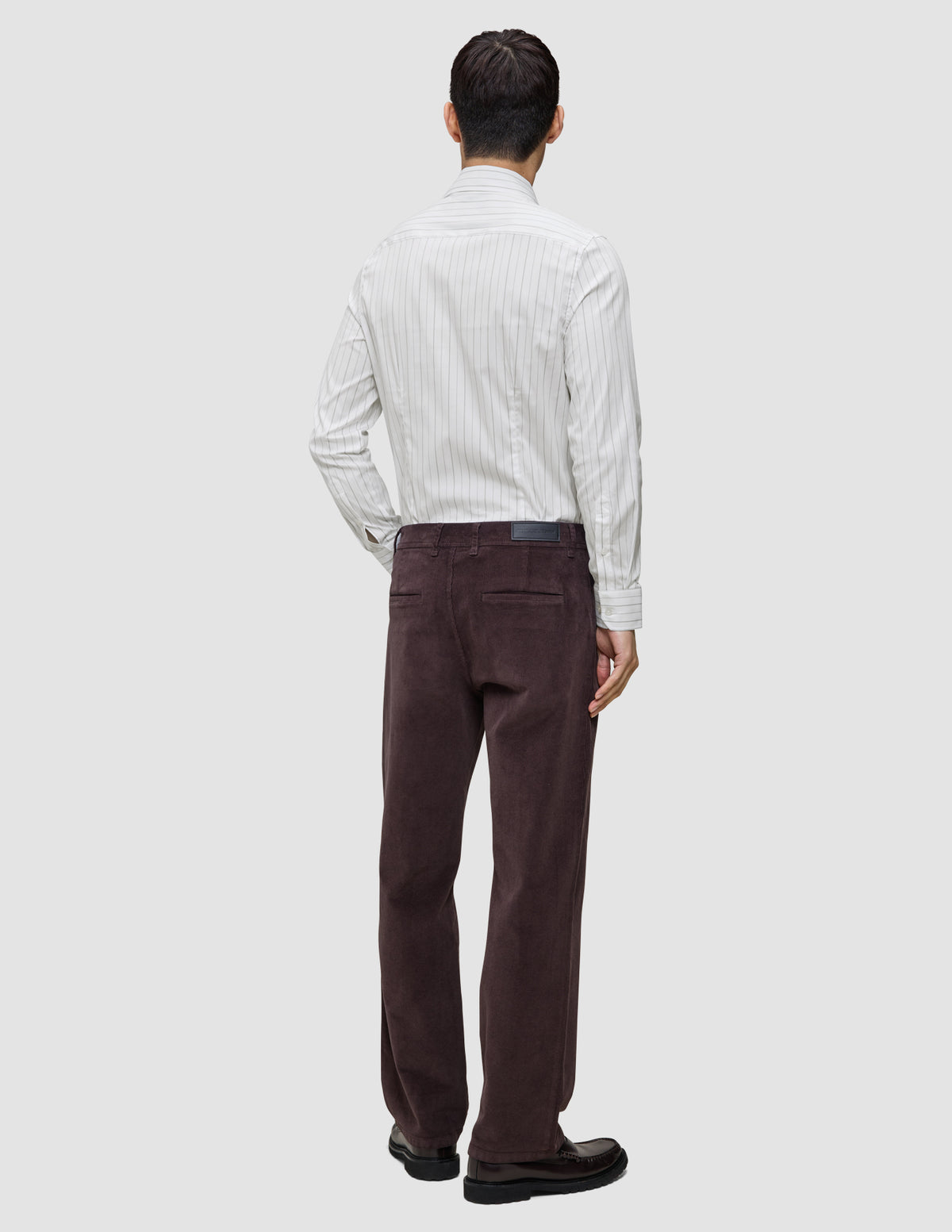 En person sett bakfra, kledd i en Elevated Shirt Slim med lysegrå striper og mørkebrune bukser.