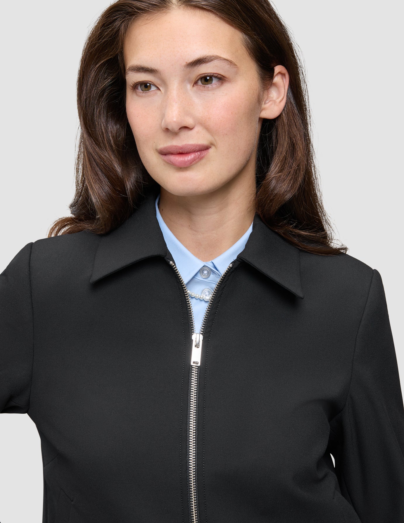 En kvinne har på seg en svart Essential Short Zip Jacket over en lyseblå skjorte med krage.