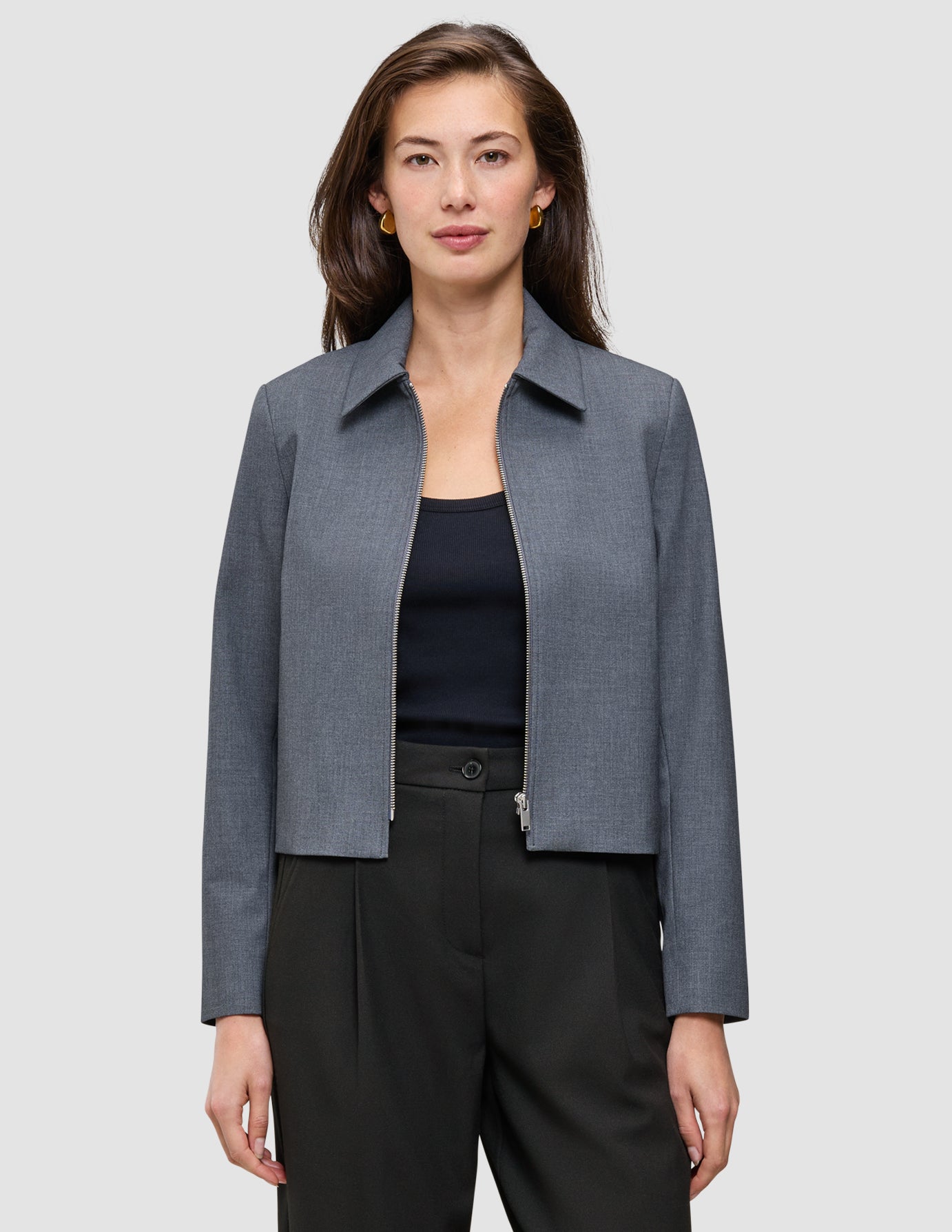 En kvinne har på seg en Essential Short Zip Jacket Dark Grey Melange – en minimalistisk jakke med krage og glidelås – over en svart topp.