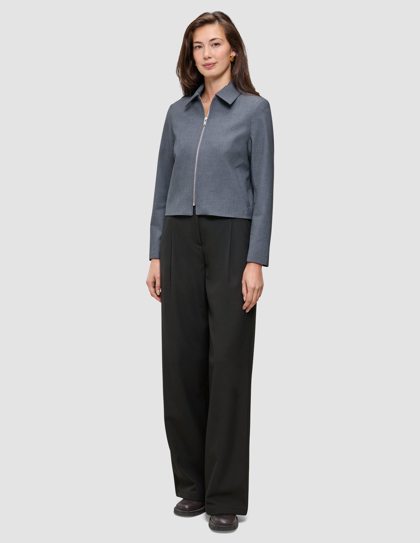 En kvinne iført en Essential Short Zip Jacket i mørkegrå melange, kombinert med svarte bukser.