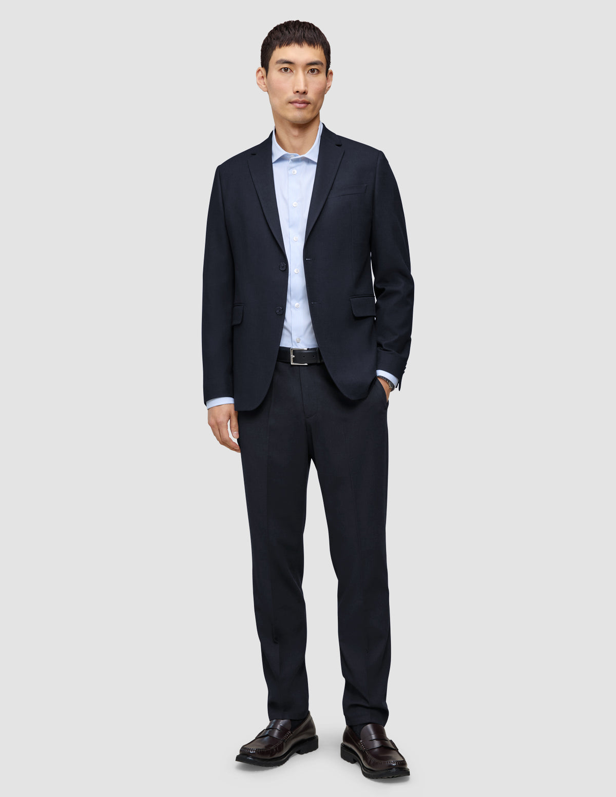 En mann har på seg en Motion Blazer Regular i fargen Midnight Blue med matchende bukser, en lyseblå skjorte og brune skinnloafers.