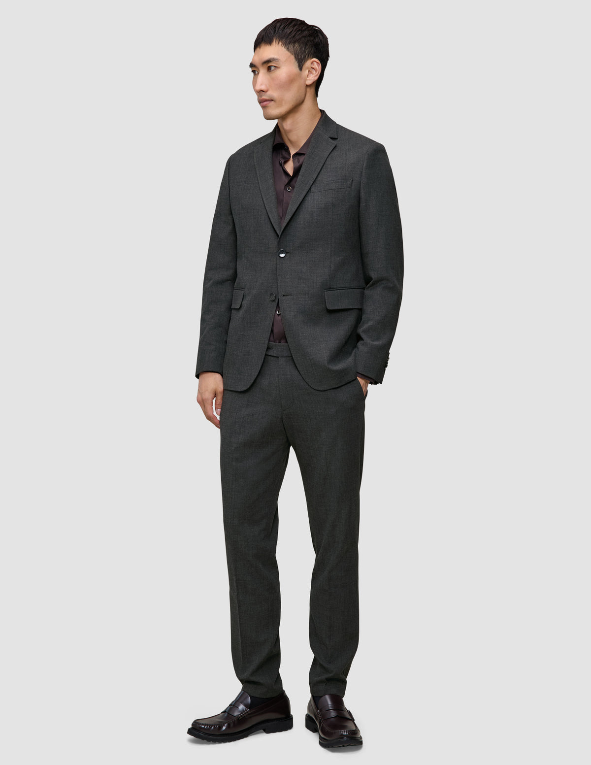 En mann kledd i en Motion Blazer Regular i fargen Pepper Grey og matchende bukser, sammen med en mørk skjorte med knapper.
