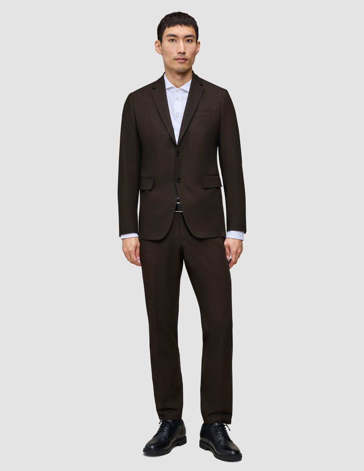En mann kledd i en mørkebrun Motion Blazer Slim Cognac over en hvit skjorte med krage og svarte dressko.