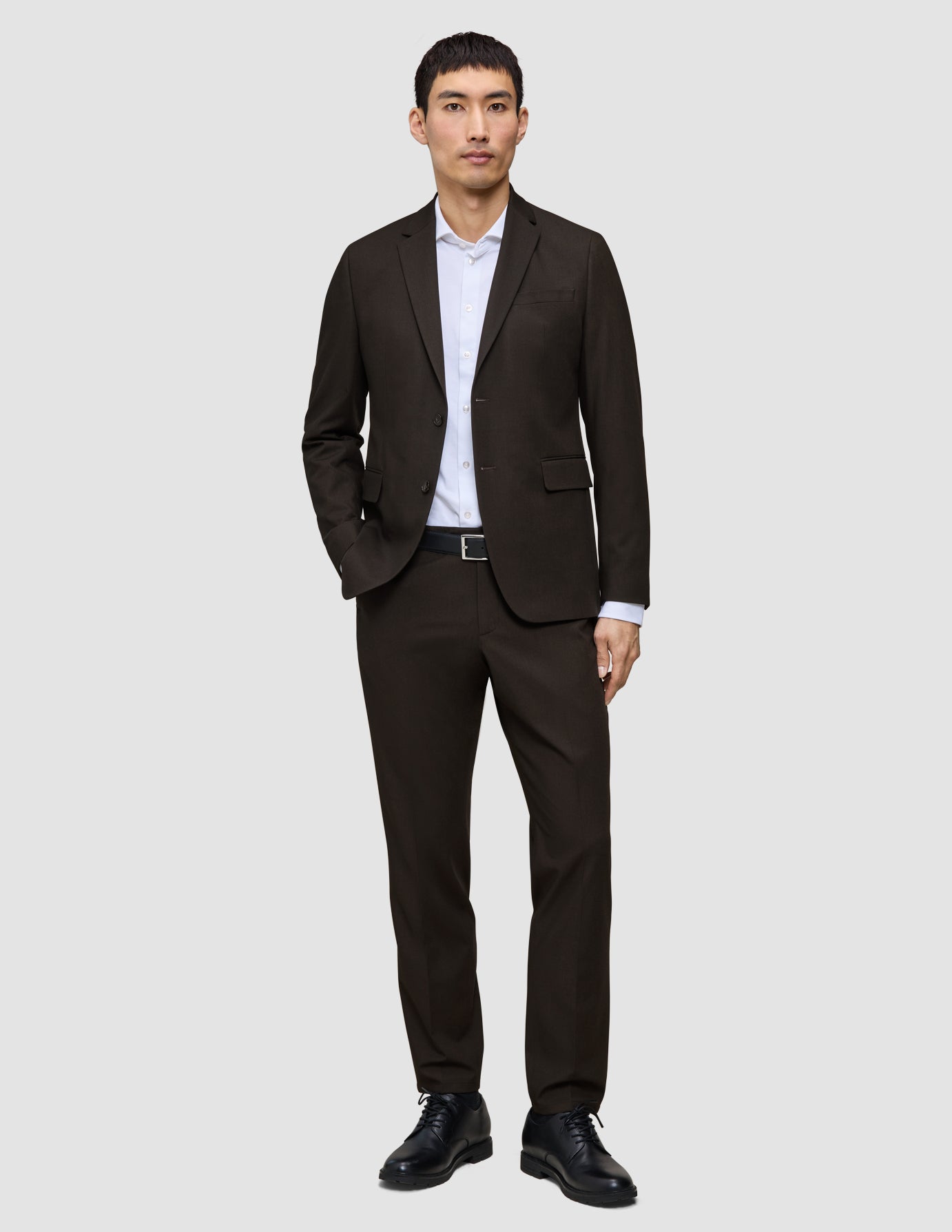 En mann kledd i en Motion Blazer Slim Cognac, hvit skjorte, svart belte og svarte dressko.